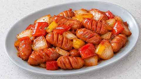 회색 접시에 담긴 칼집 낸 비엔나소세지와 빨간색·노란색 채소 볶음